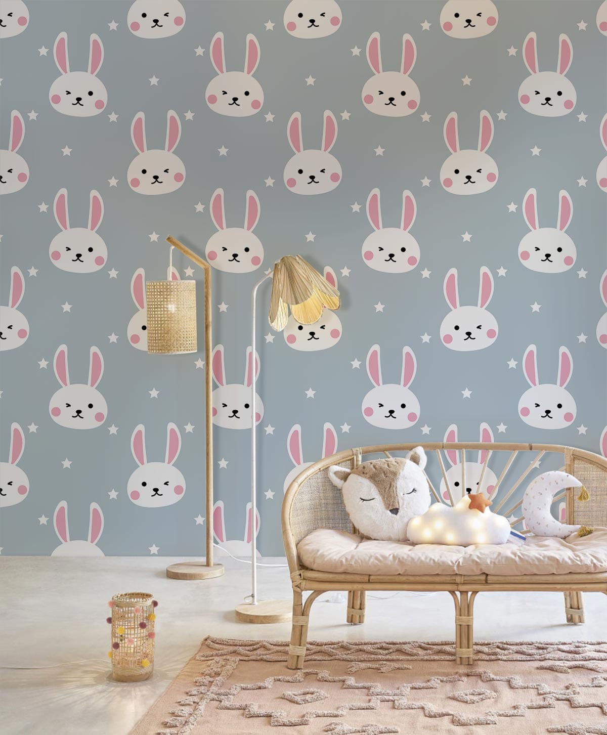Whimsical Bunny wallpaper in pastel blue nursery with rattan sofa, plush cushion, and woven rug.