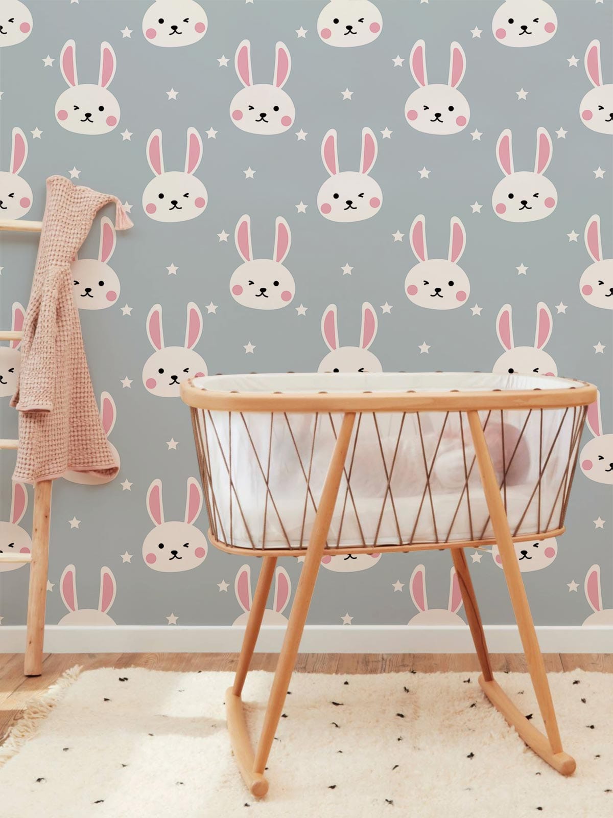 Soft pastel blue bunny wallpaper in nursery with wooden crib and cream rug. Whimsical, playful decor.