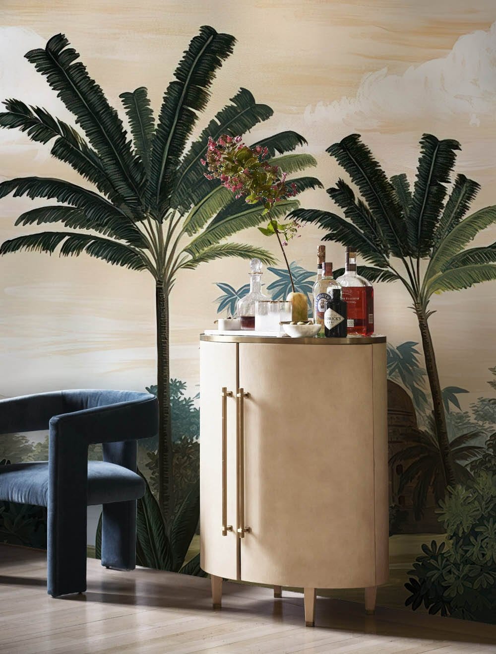 Tropical vintage palm mural wallpaper in earthy tones with blue velvet chair and wood flooring.