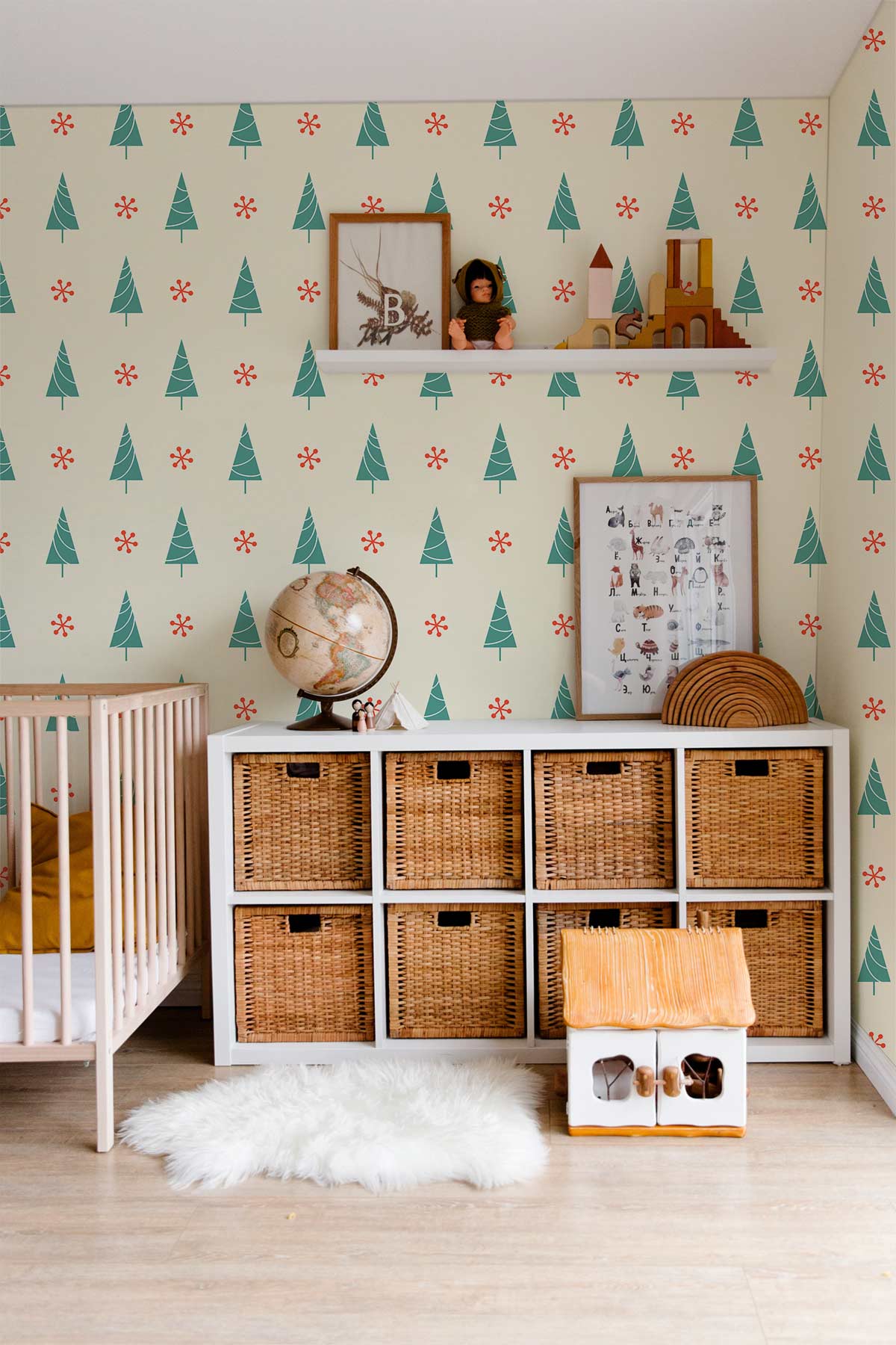 Festive evergreen Christmas tree wallpaper in nursery with wicker baskets, light wood flooring, and cot.
