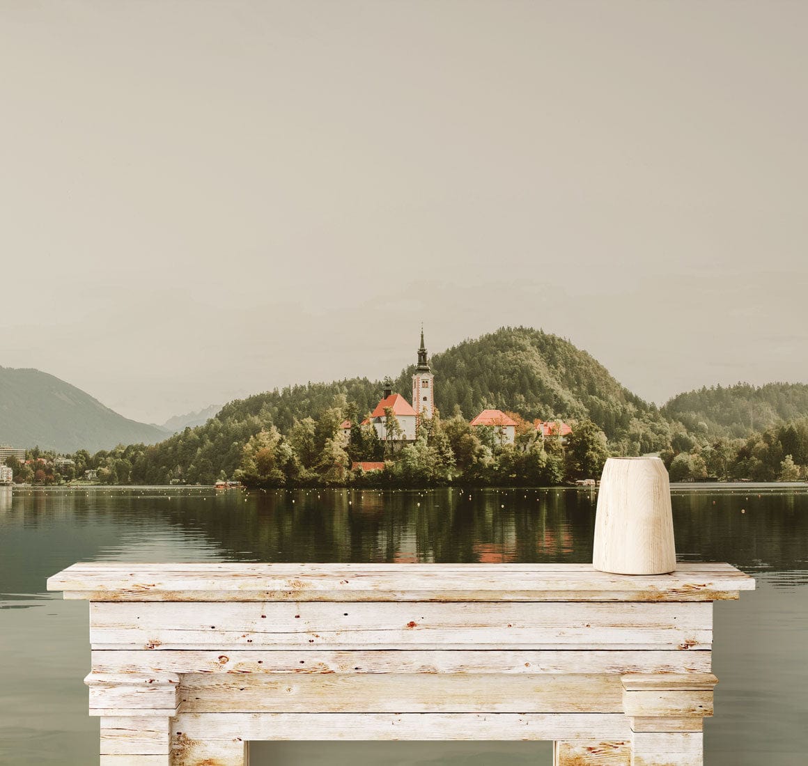 Tranquil Lakeside Village Mural enhances rustic table, capturing serene landscape. Ideal for living room.