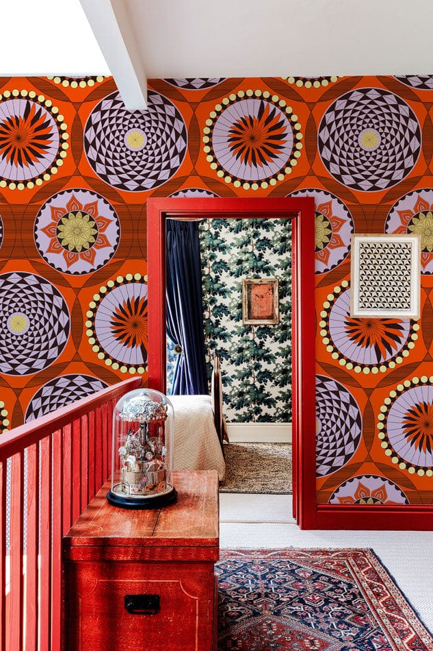 Vibrant geometric retro wallpaper with bold orange and black design, red railing, rug, and textured flooring.