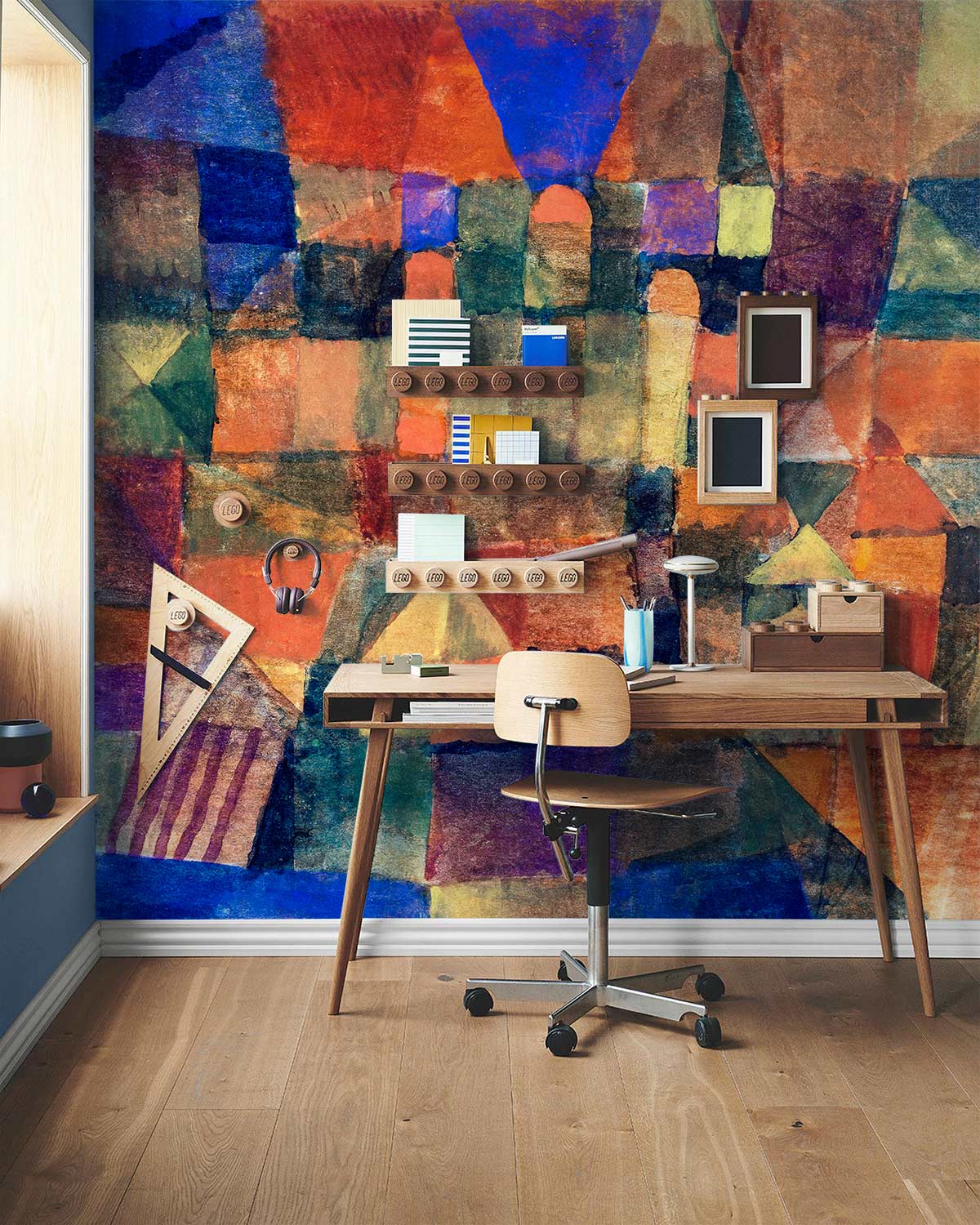 Vibrant geometric mural wallpaper with wooden desk, chair, and decor in striking contemporary abstract design.