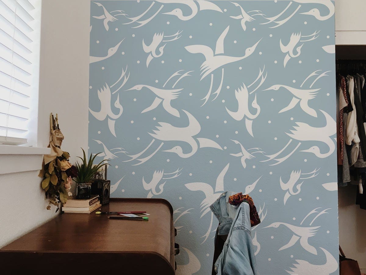 Blue and white crane silhouette patterned wallpaper in stylish room with wooden desk, window blinds.