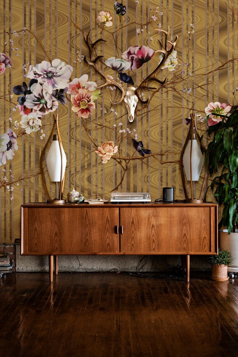 Elegant floral wallpaper with gold botanical design, vintage wooden sideboard, rich wood flooring, lamps.