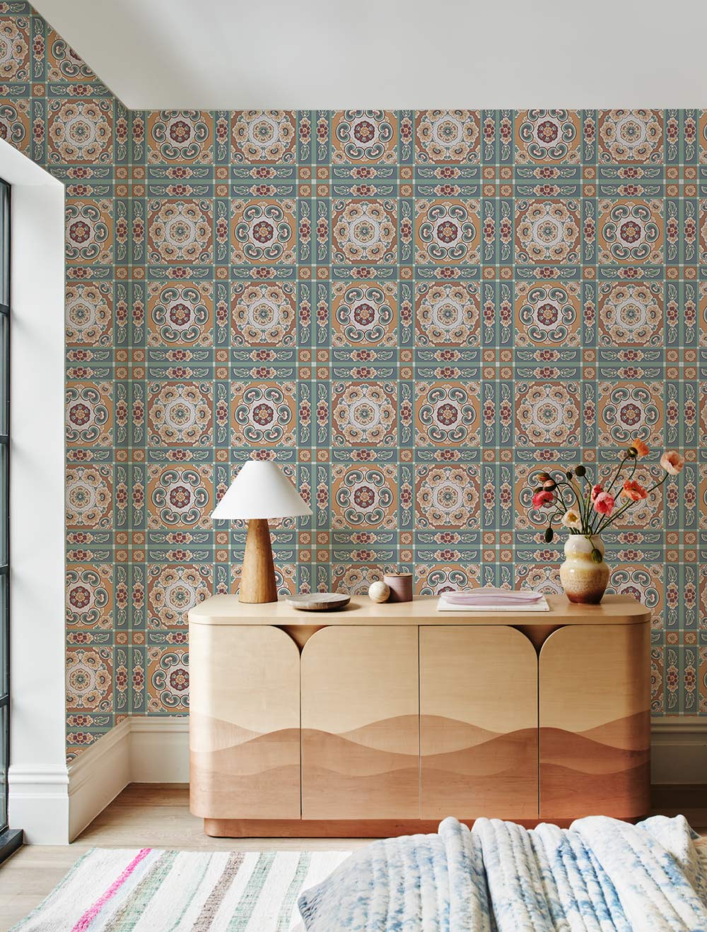 Vintage Mediterranean tile wallpaper with turquoise tones, wooden sideboard, striped rug, stylish lamp.