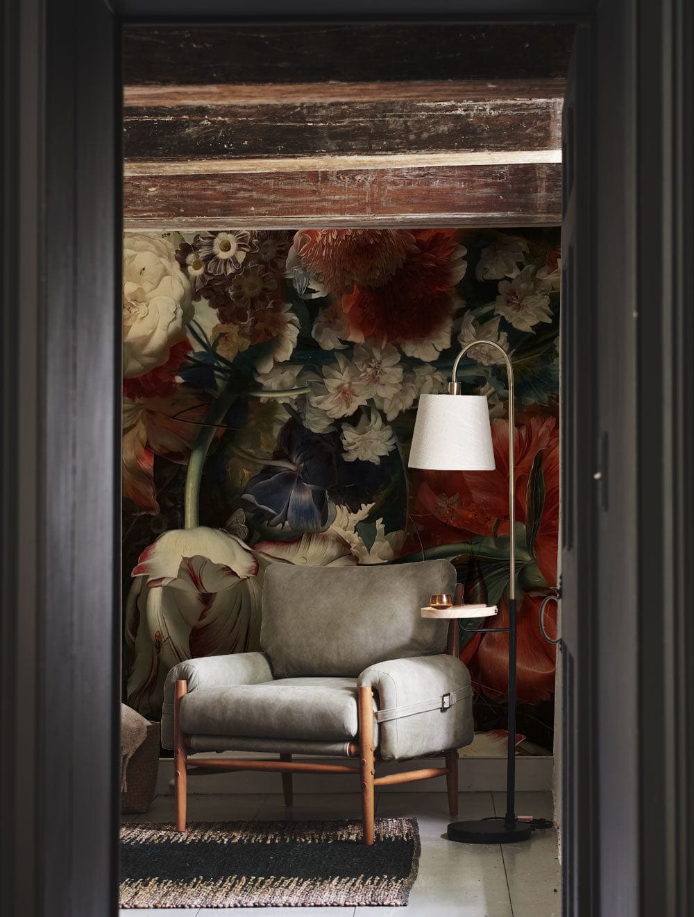 Vintage floral mural wallpaper with dark botanical design featuring grey armchair and rustic flooring.