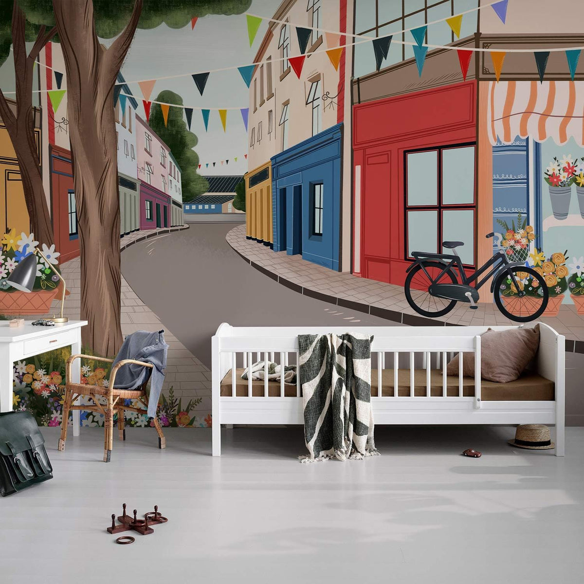 Charming vintage village street mural wallpaper in kids' room; white bed, wooden chair, grey floor.