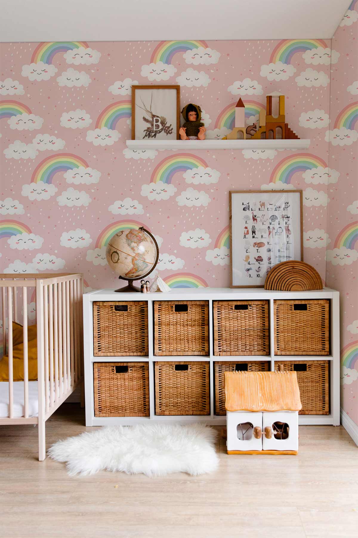 Dreamy pink rainbow nursery wallpaper, wicker storage, white crib, light wood flooring in child's room.