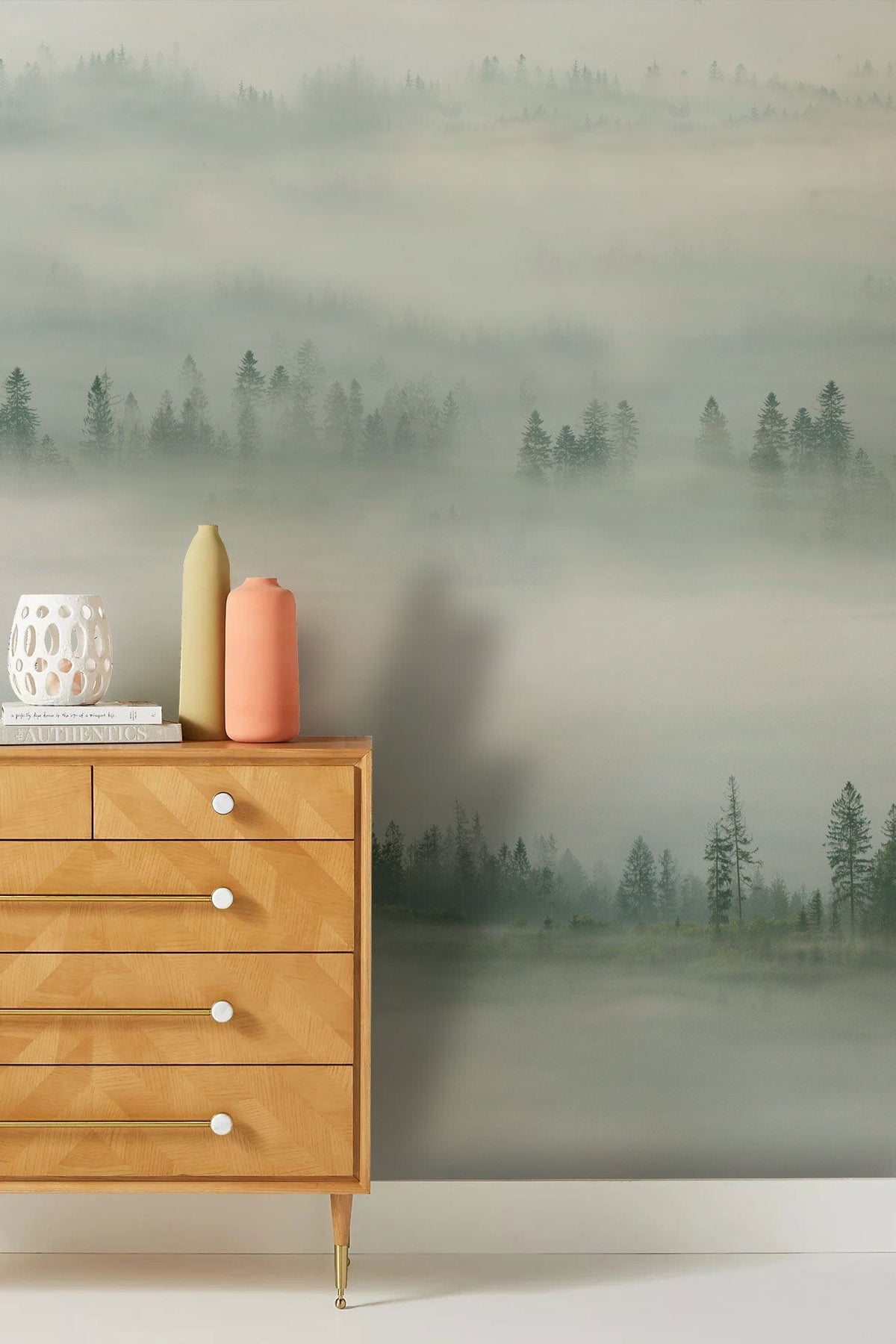 Tranquil misty forest wallpaper in grey tones, wooden chest of drawers, soft white flooring.