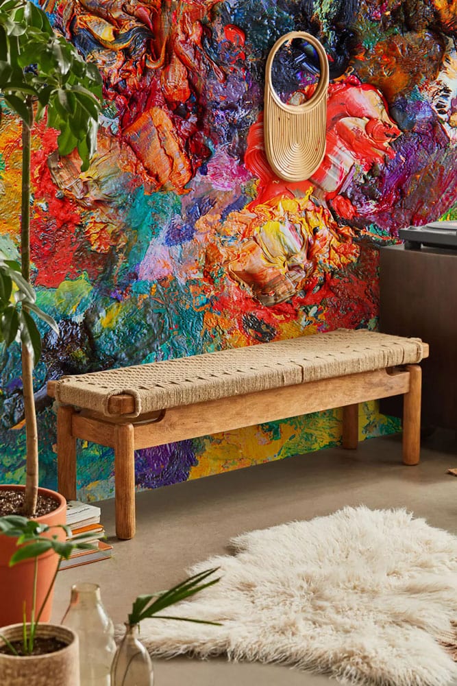 Vibrant abstract colourful mural wallpaper, natural wood bench, textured rug, and green decor in modern interior.