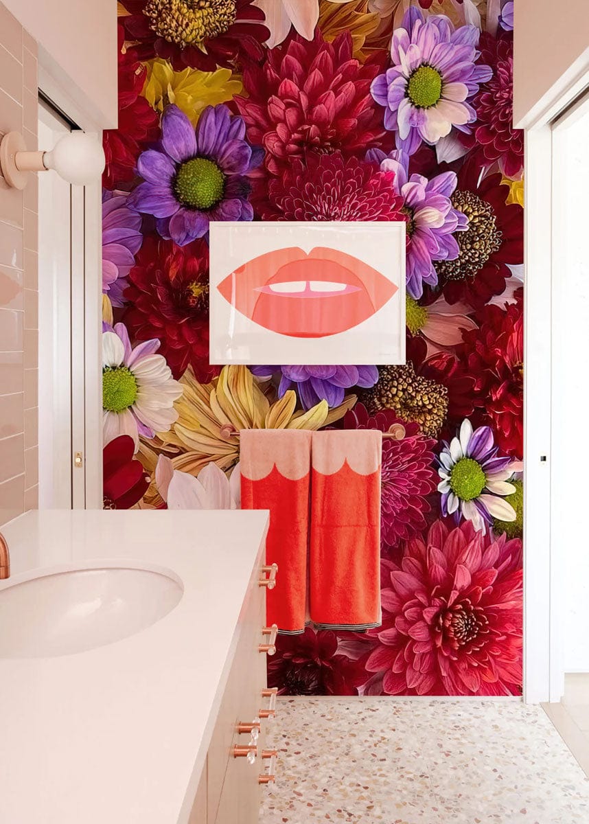 Vibrant multicolour floral wallpaper in stylish bathroom with terrazzo flooring, modern artwork, and orange towels.