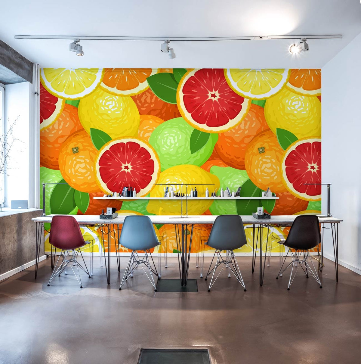 Vibrant citrus fruit wallpaper in kitchen, colourful chairs, modern bar-style table, concrete flooring.