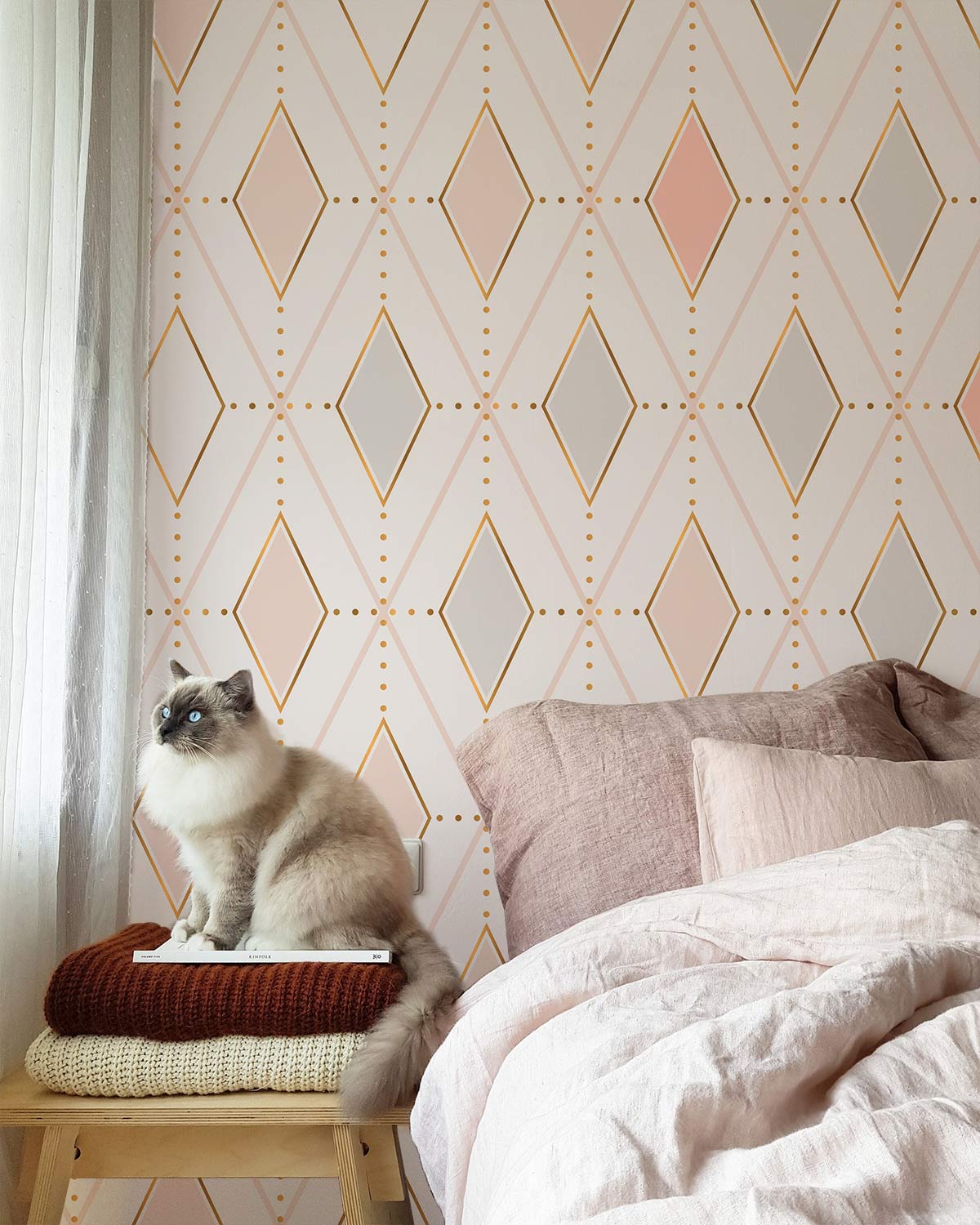 Geometric pastel diamond wallpaper with soft pink bedding, grey tones, and cat in a cosy bedroom.