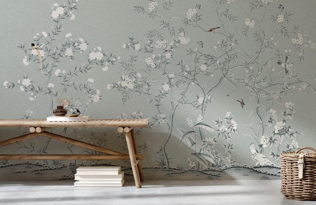 Elegant Chinoiserie garden mural wallpaper, muted green tones, rustic bench, wicker basket, light flooring.