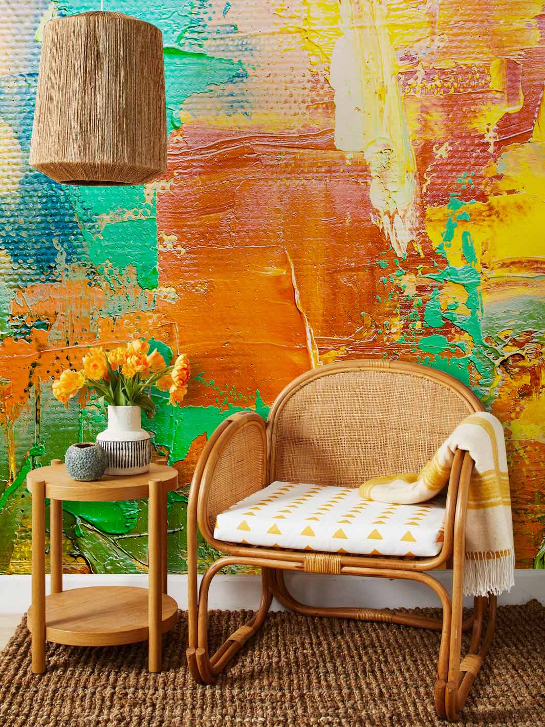 Vibrant abstract mural with bold yellow-orange-green design, wicker chair, jute rug, wooden side table.