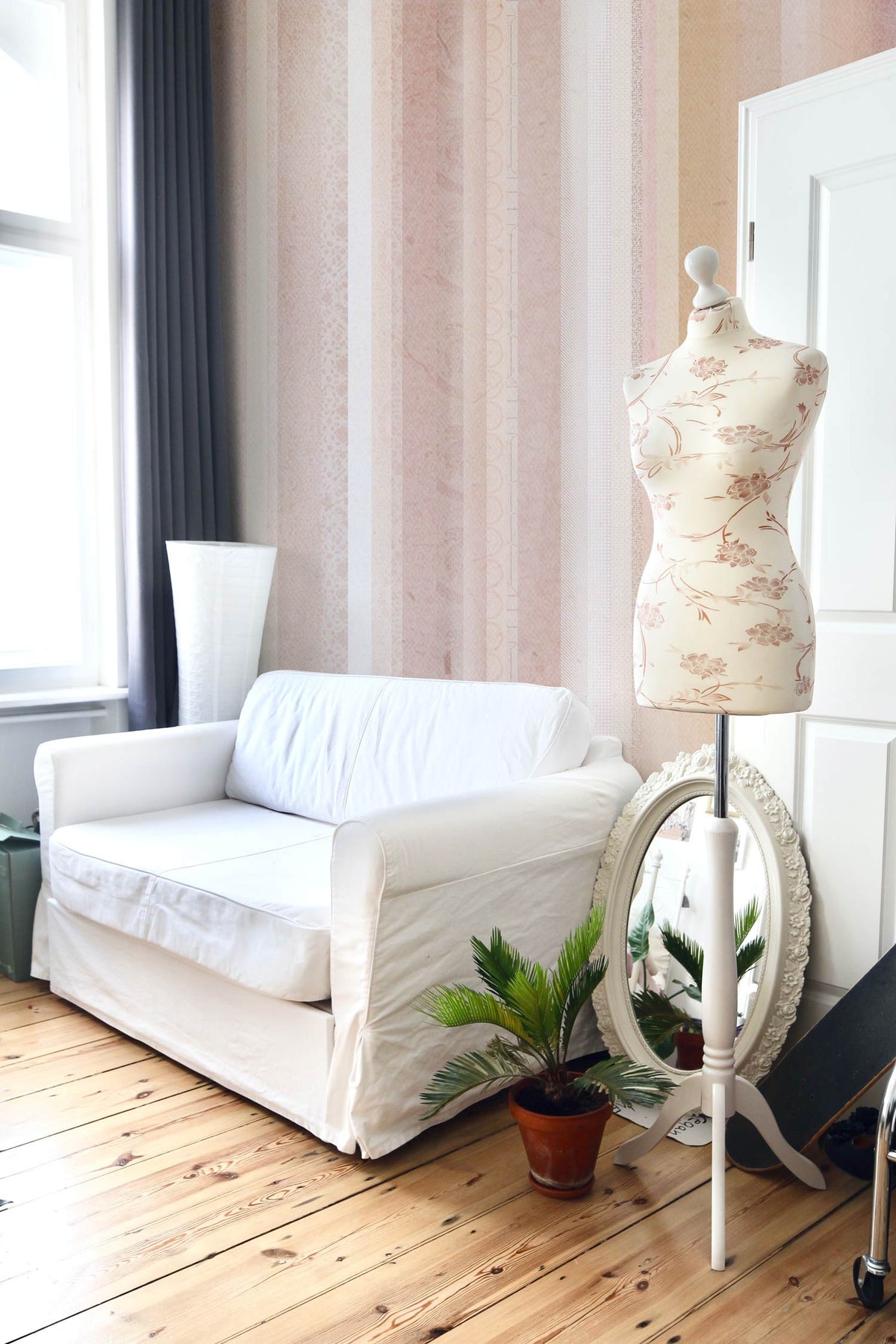 Pastel stripes wallpaper, white sofa, mannequin, light wood flooring, elegant living room setting.
