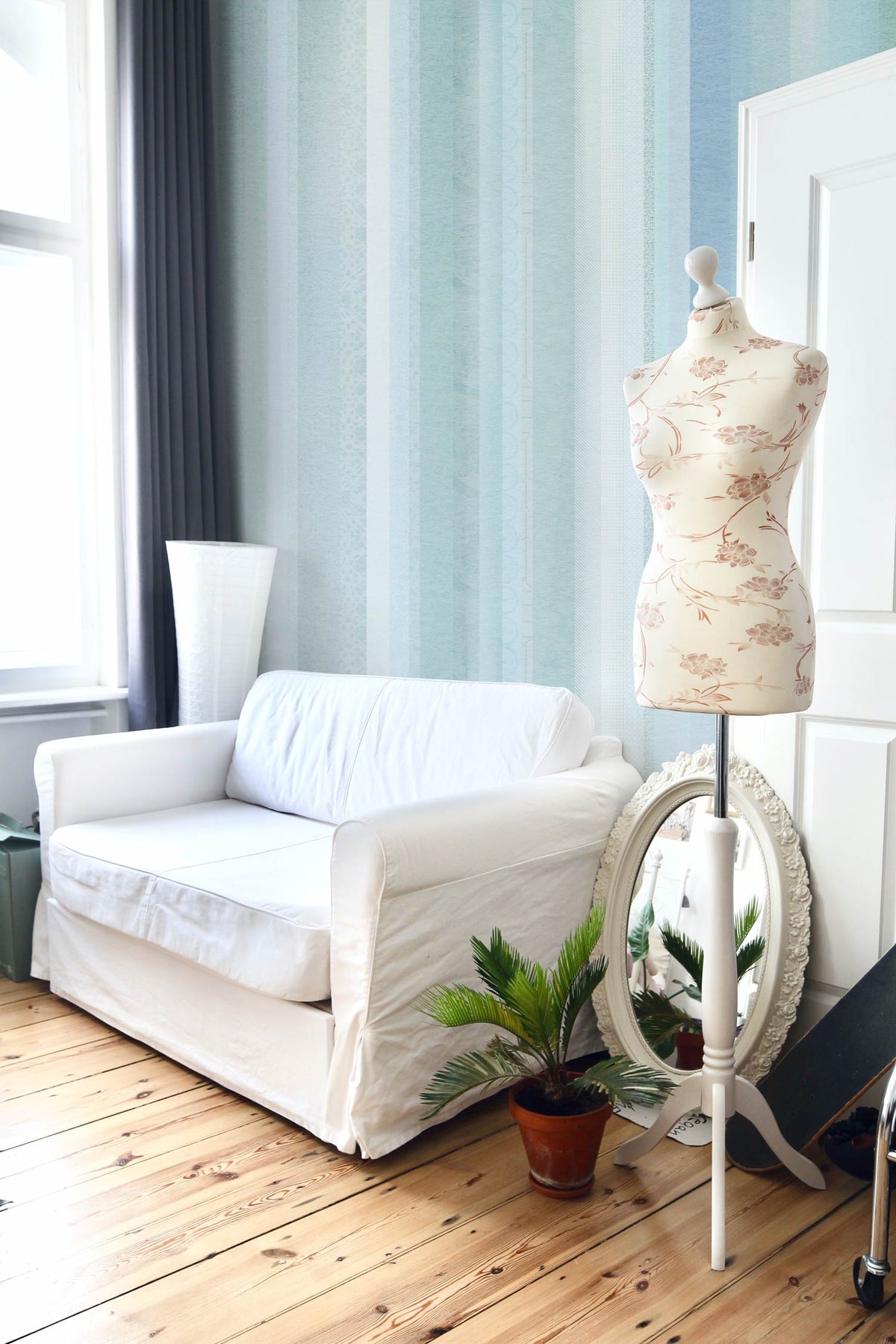 Pastel Stripes wallpaper with mannequin, white sofa, wooden flooring, and decorative plant in modern room.