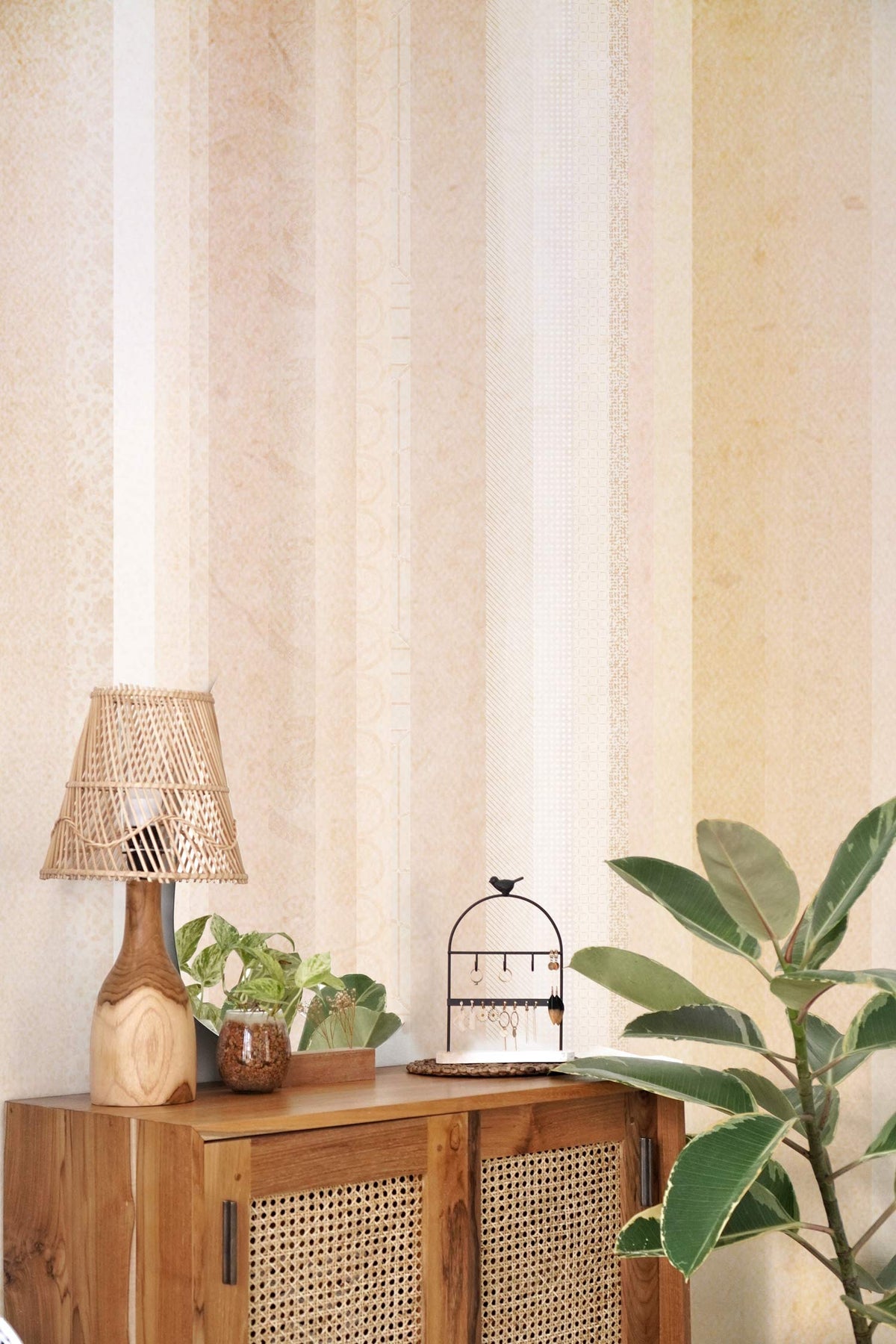 Pastel vertical stripes wallpaper with beige, blue hues; wooden cabinet, wicker lamp, indoor plant.