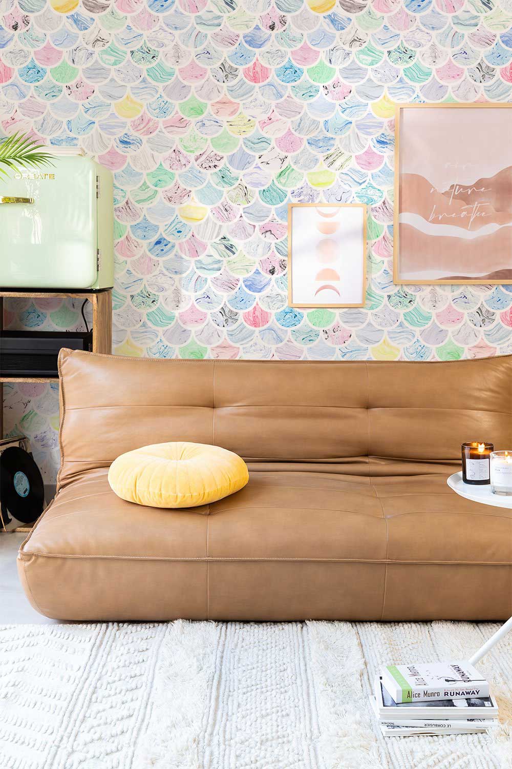 Pastel seashell wallpaper in lounge with brown leather sofa, mustard cushion, and light rug flooring.