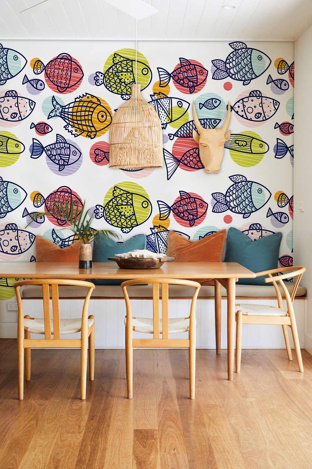 Colourful fish-patterned wallpaper in kids' room with wooden dining table, chairs, and vibrant cushions.