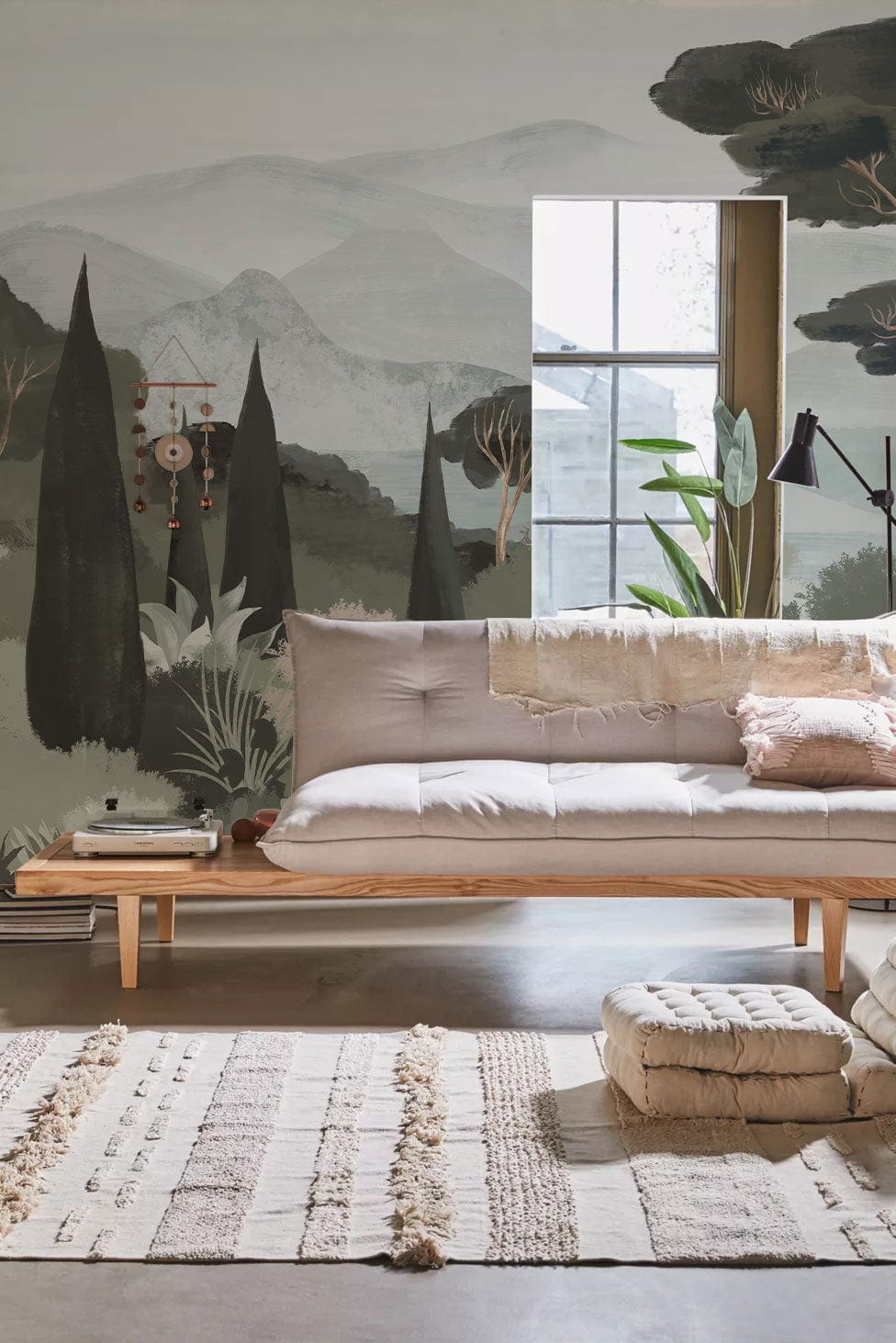 Tranquil Evergreen Landscape Mural with beige sofa, rustic wooden flooring, and bohemian pouffe in living room.