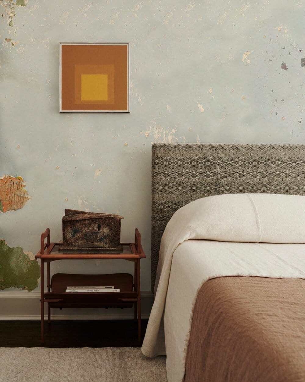 Vintage soft blue wall mural, distressed texture, rustic bedroom decor, cosy bed, wooden nightstand.