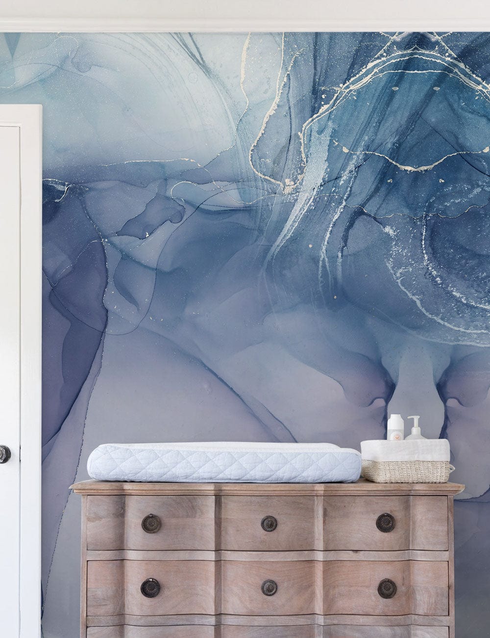 Elegant blue watercolour abstract mural wallpaper with marble effect behind rustic wooden chest in bedroom.