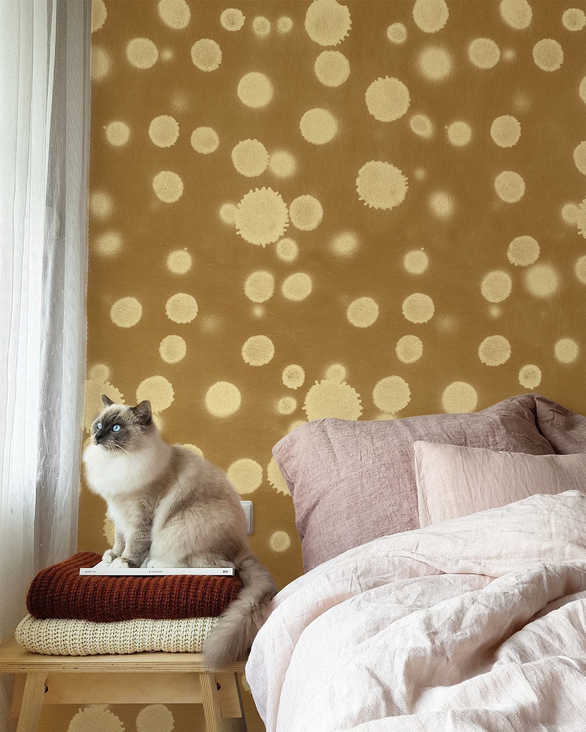 Vintage polka dot wallpaper, warm tones, cosy interior, soft pink bedding, cat on wooden stool.