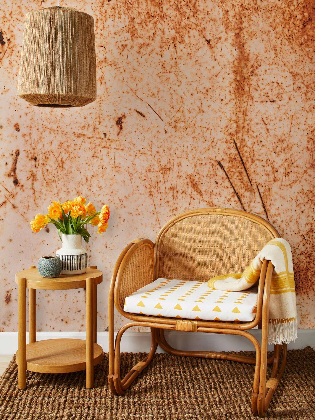 Vintage rust texture mural wallpaper, rustic rattan chair, neutral woven lampshade, side table, textured rug.
