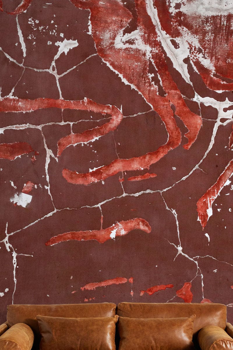 Rustic red cracked earth mural wallpaper in cosy living room with brown leather sofa for interiors.