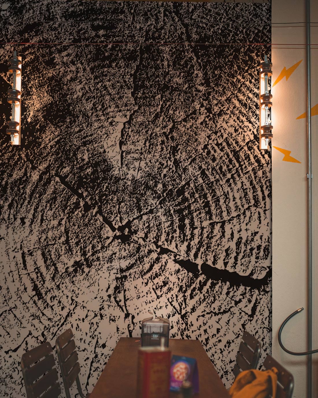 Monochrome Tree Rings wallpaper in dining room with rustic chairs, wall lights, and industrial decor elements.