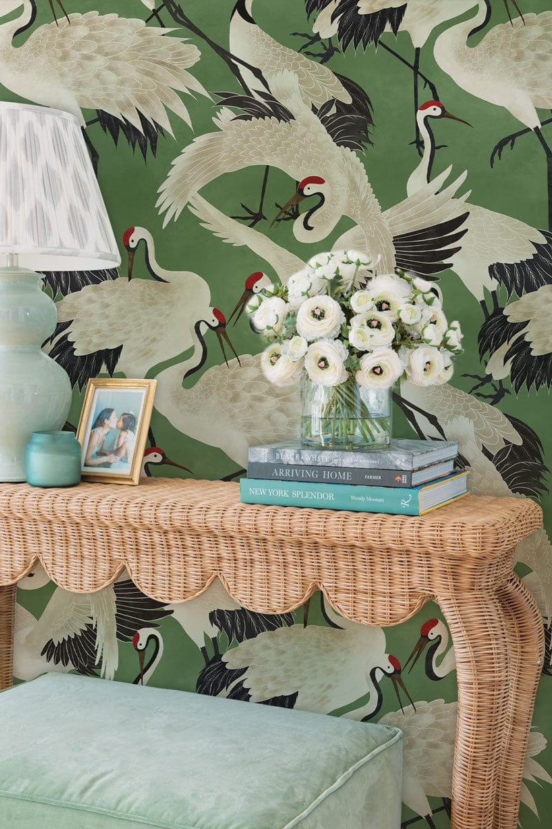 Elegant Green Crane Motif Wallpaper, rattan console table, pastel lamp, velvet stool, floral arrangement.
