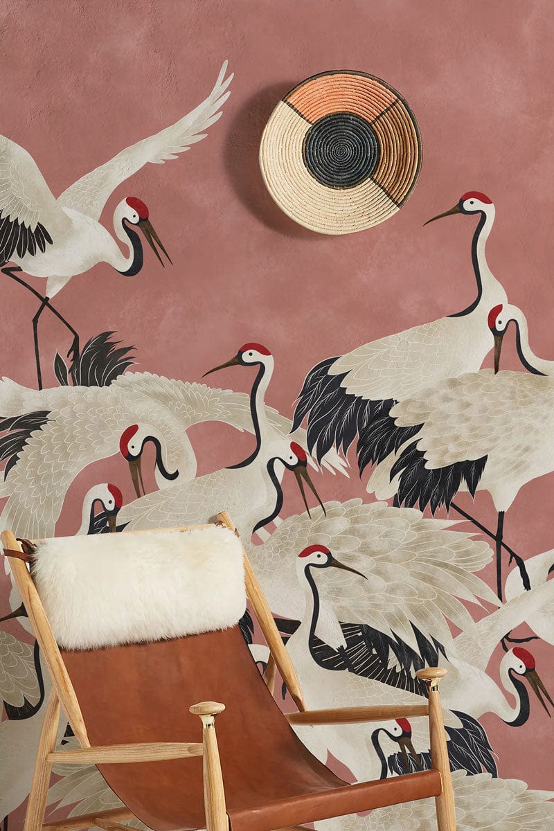 Luxurious coral wallpaper featuring cranes, wooden chair with fur overlay, woven decor item on wall.
