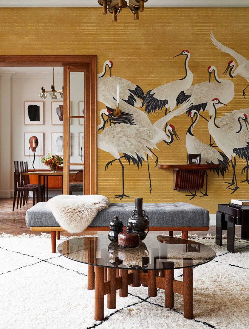 Elegant Golden Crane Mural Wallpaper adorns dining room with grey sofa, chic rug, and wooden furniture.