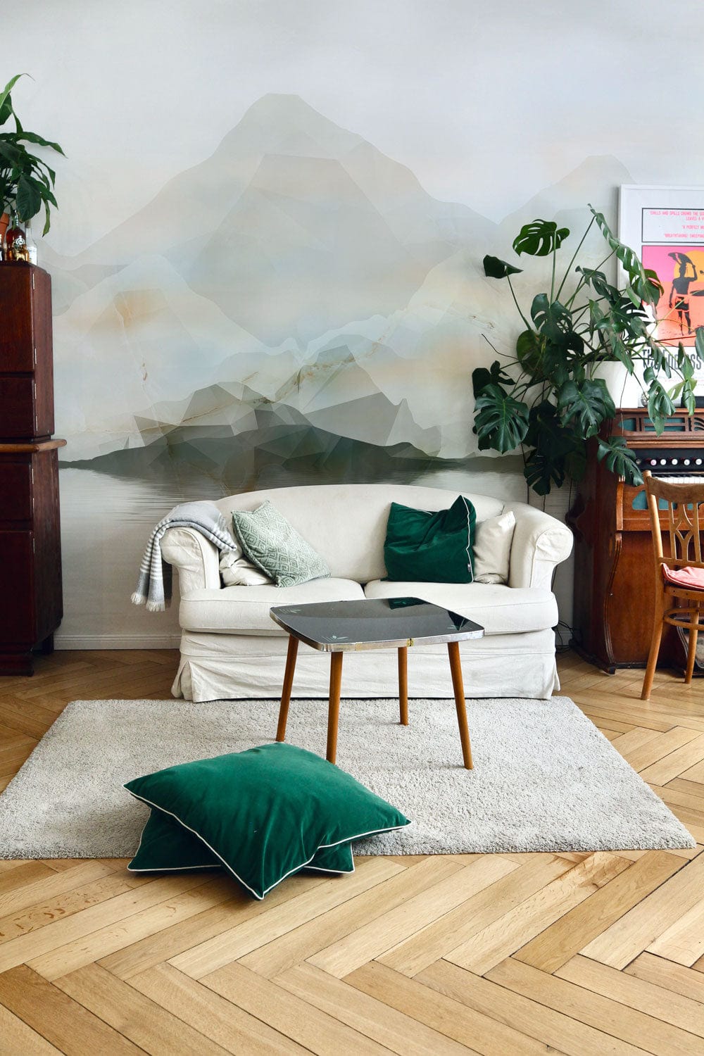 Tranquil Watercolour Mountain Mural Wallpaper in neutral tones, cosy white sofa, green cushions, parquet flooring.