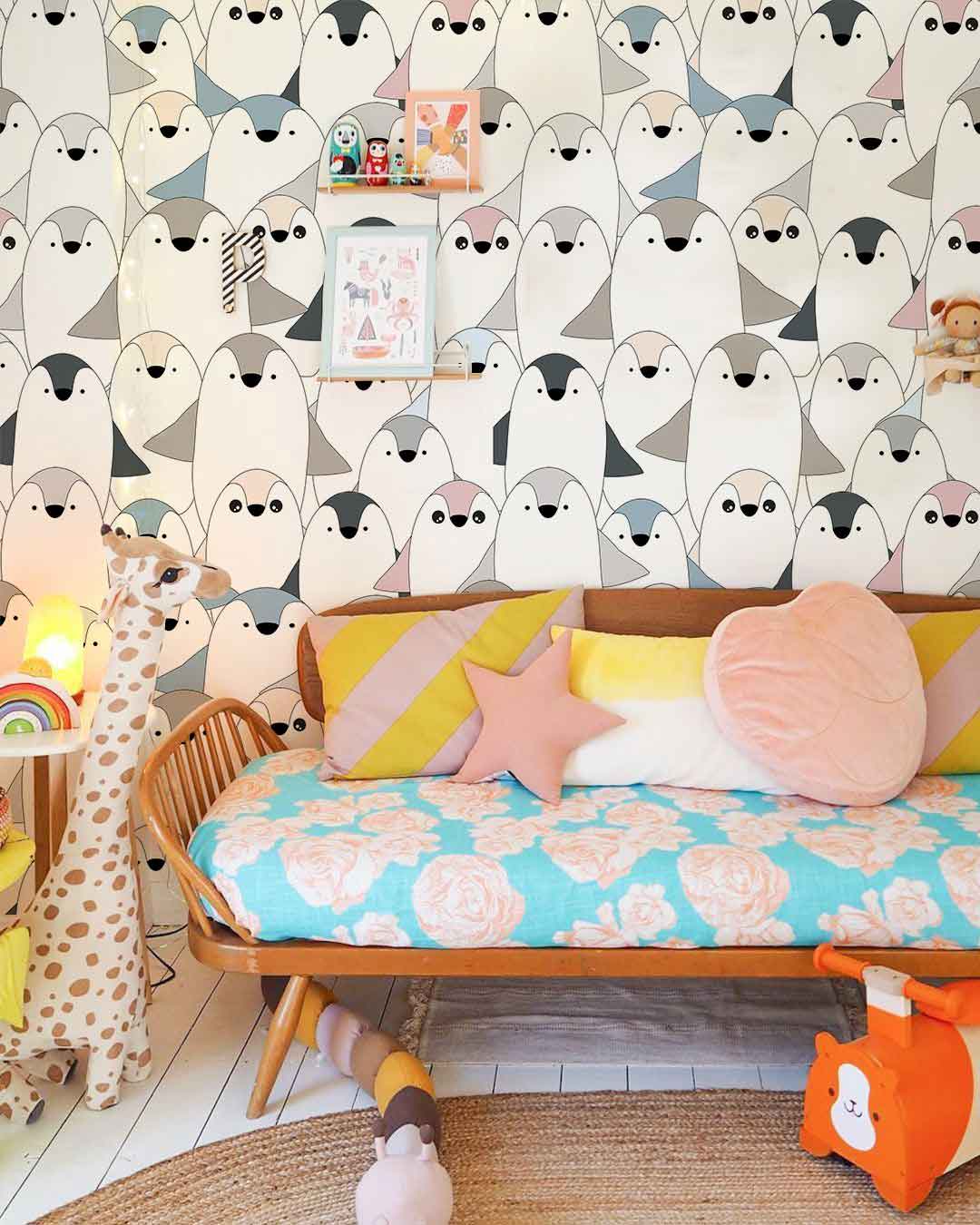 Adorable pastel penguin wallpaper; wooden bench, colourful cushions, nursery decor, giraffe toy, light flooring.