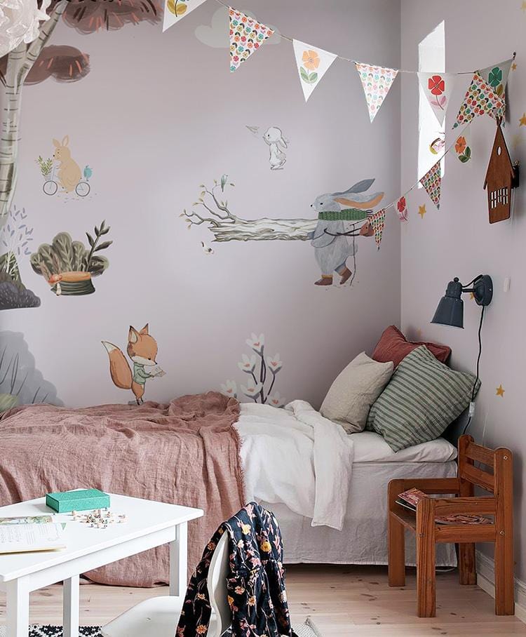 Children's room with whimsical woodland mural, pastel animals, wooden chair, white table, cosy bedding.