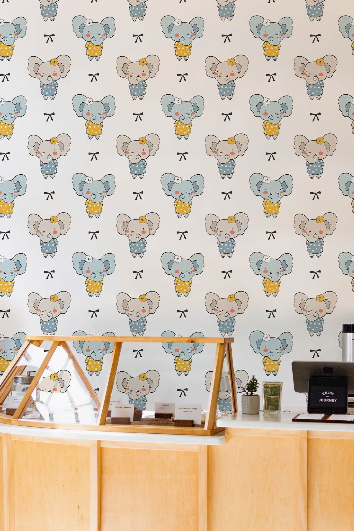 Charming Elephant Wallpaper for Nursery, pastel blue design, light wood counter, cheerful decor.