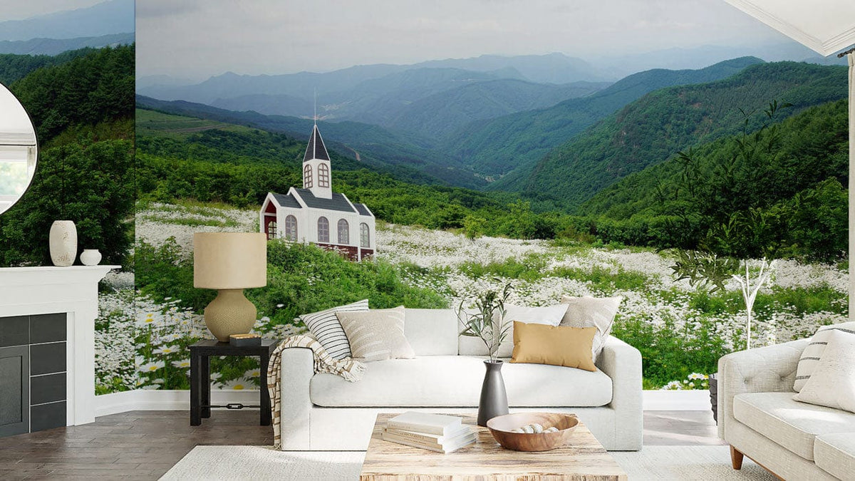 Charming mural wallpaper featuring countryside church in meadow; white sofa, wooden table, serene living room.