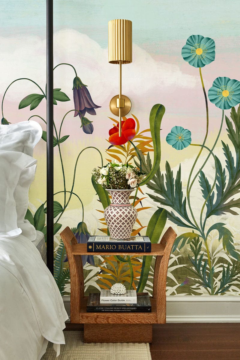 Bedroom with colourful floral wallpaper behind a wooden bedside table and unique gold wall lamp.