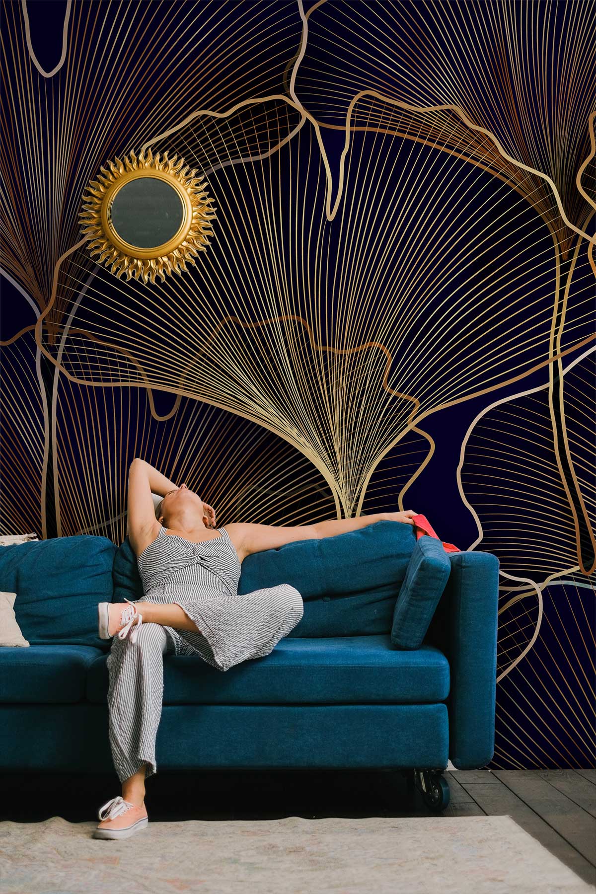 Elegant gold navy leaf wallpaper, teal sofa, dark wood flooring, sunburst mirror, sophisticated room design.