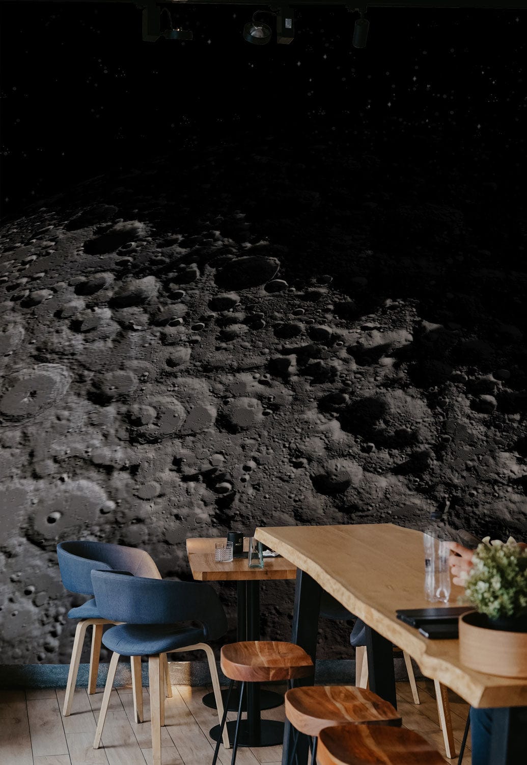 Moonlit Crater Landscape Wallpaper decorates coffee shop with wooden tables, blue chairs, light flooring.