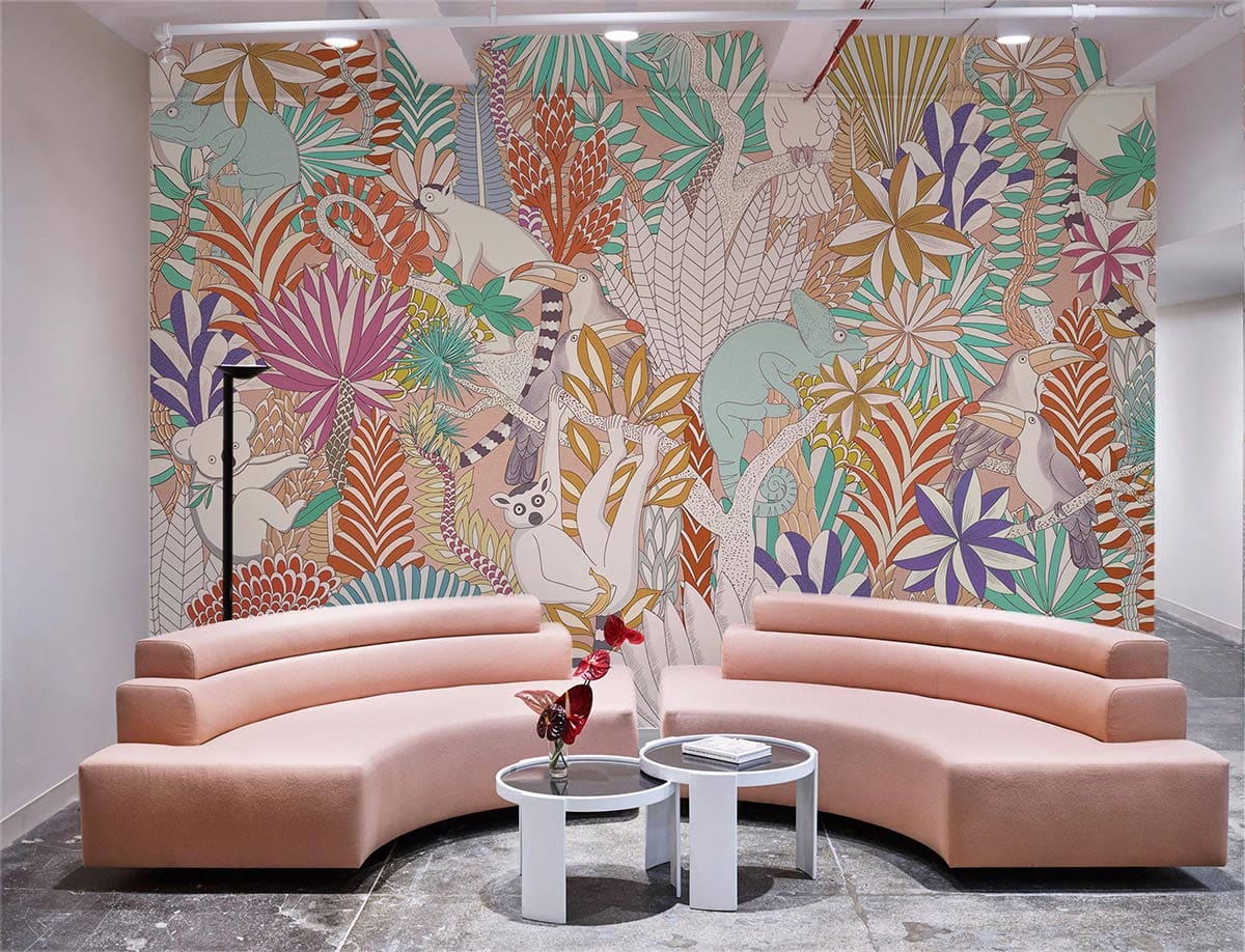 Tropical Jungle Animals colourful mural with bohemian design, curved peach sofas, round tables, concrete floor.