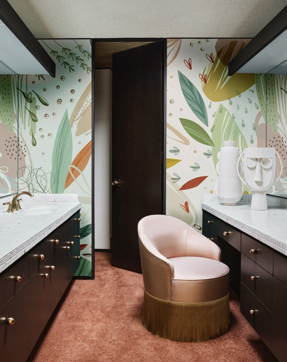 Abstract Botanical Pastel Wallpaper in earthy tones adorns bathroom with pink velvet chair and brown cabinets.