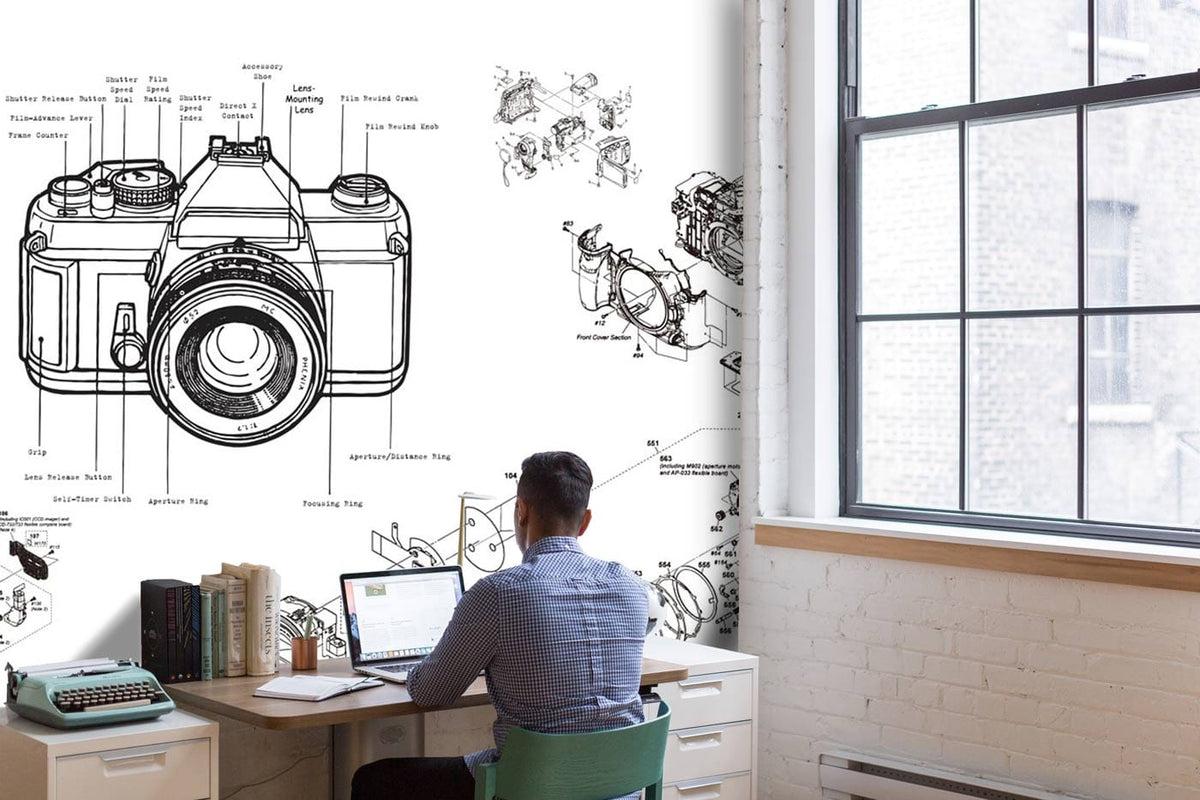 Man at desk with vintage camera blueprint mural, black and white industrial wallpaper, modern office.
