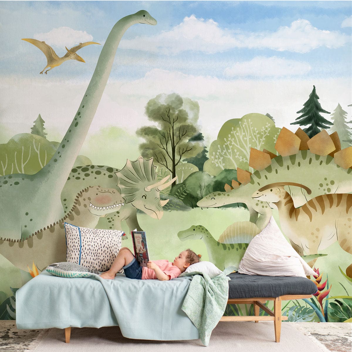 Colourful children's dinosaur mural wallpaper on wall; features dinosaurs. Child relaxing on blue sofa.