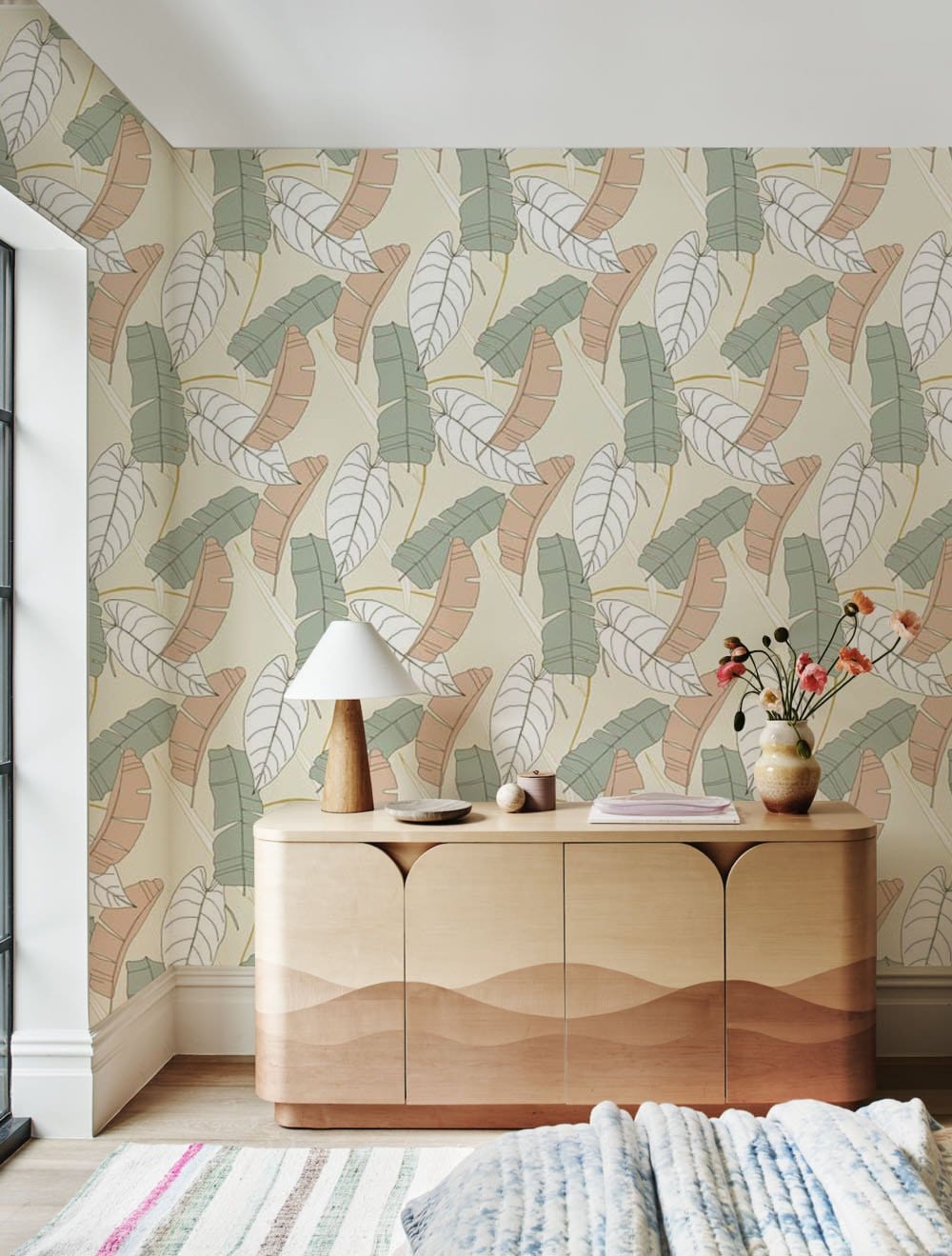 Botanical pastel leaf wallpaper in soft green and beige with modern wood cabinet, striped rug.