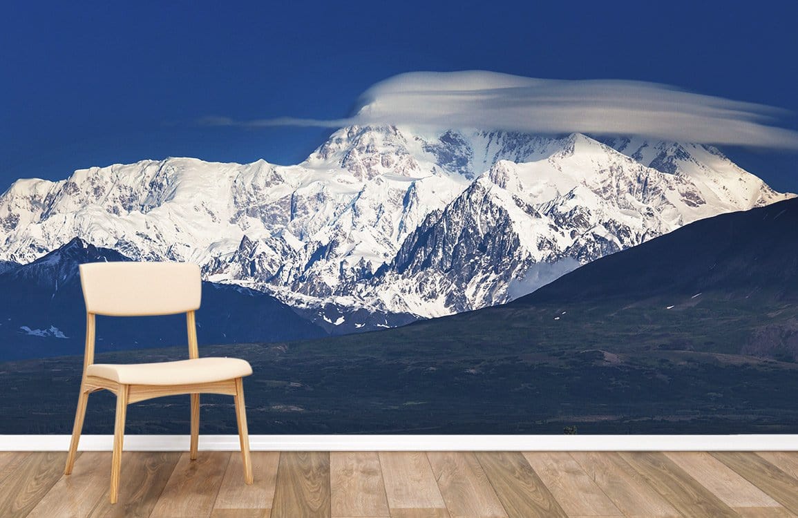 Majestic snowy mountain mural wallpaper with beige chair, wooden flooring, blue sky, serene decor.