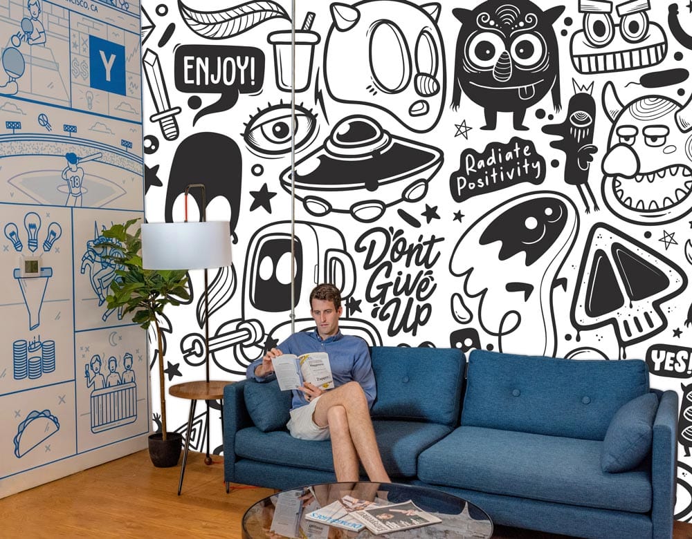 Monochrome Quirky Doodle Mural Wallpaper with blue sofa, wood flooring, and lamp in creative room.